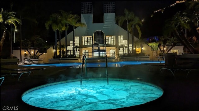 pool at twilight featuring a hot tub and a community pool