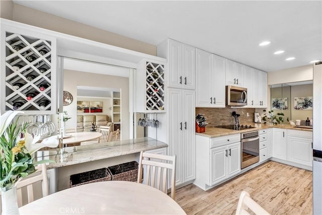 kitchen with stainless steel appliances, light wood finished floors, white cabinetry, light stone counters, and recessed lighting