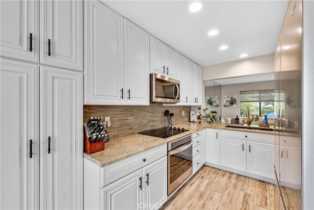 kitchen featuring appliances with stainless steel finishes, light wood-type flooring, a sink, white cabinets, and backsplash