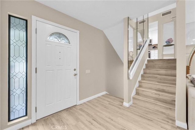 entryway featuring light wood finished floors, stairway, baseboards, and vaulted ceiling