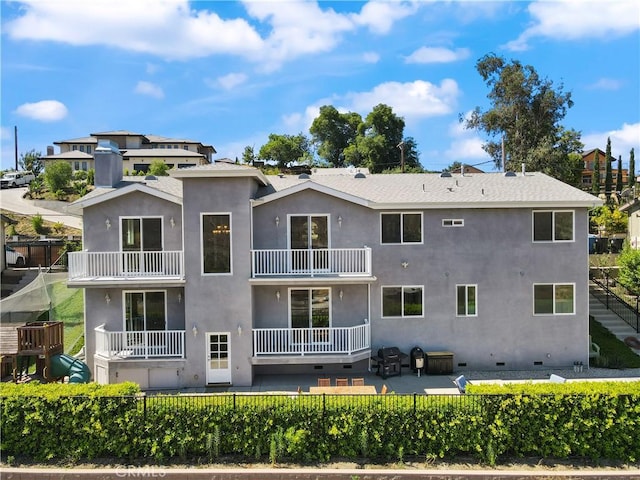 rear view of house with a balcony, stucco siding, a patio, and fence