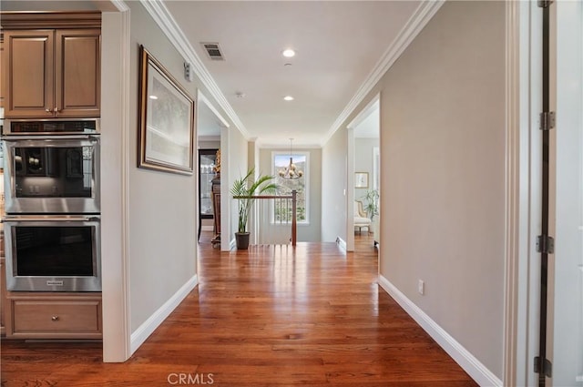 corridor with wood finished floors, a chandelier, ornamental molding, baseboards, and recessed lighting