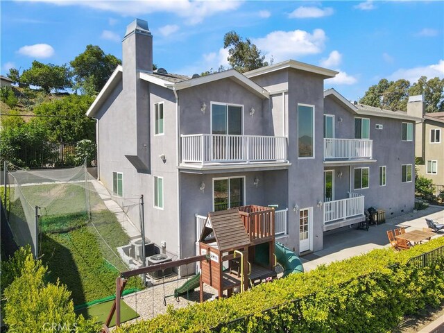 rear view of house with a chimney, stucco siding, a balcony, a patio, and cooling unit