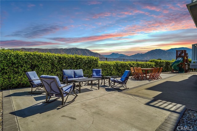 patio terrace at dusk featuring a mountain view, fence, and an outdoor living space