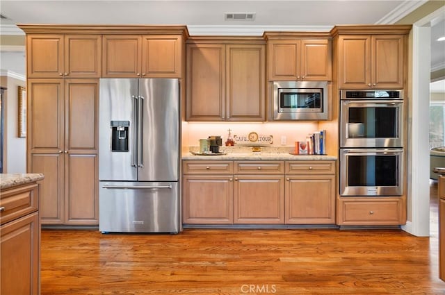 kitchen featuring stainless steel appliances, light stone countertops, light wood-style flooring, and ornamental molding