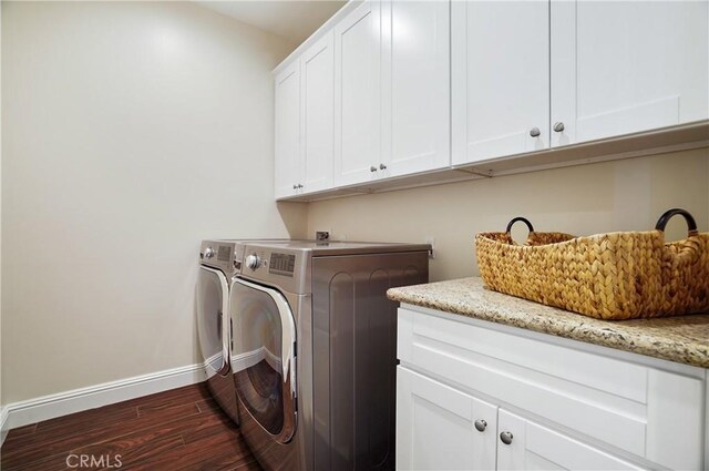 clothes washing area with cabinet space, washing machine and dryer, baseboards, and dark wood-type flooring