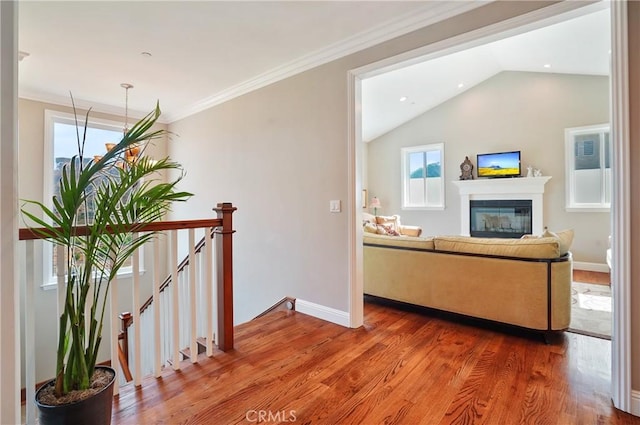 corridor with an upstairs landing, wood finished floors, vaulted ceiling, baseboards, and ornamental molding