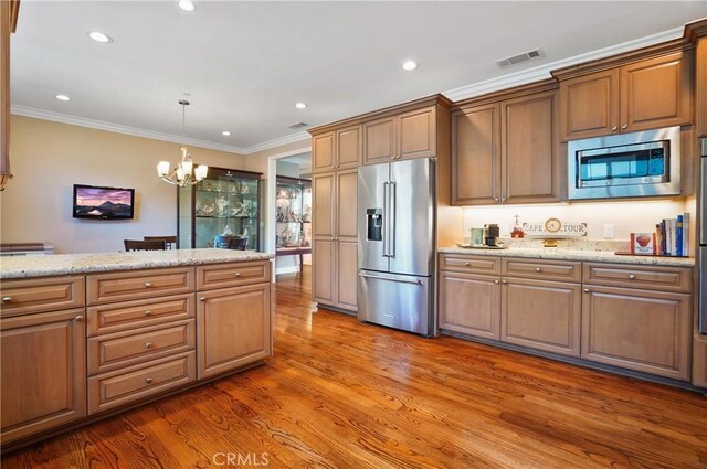 kitchen with stainless steel appliances, a chandelier, wood finished floors, ornamental molding, and recessed lighting
