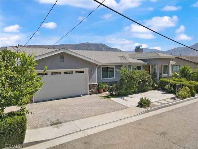 single story home featuring a mountain view, stucco siding, an attached garage, and stone siding