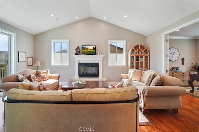 living room with wood finished floors, a glass covered fireplace, plenty of natural light, vaulted ceiling, and recessed lighting