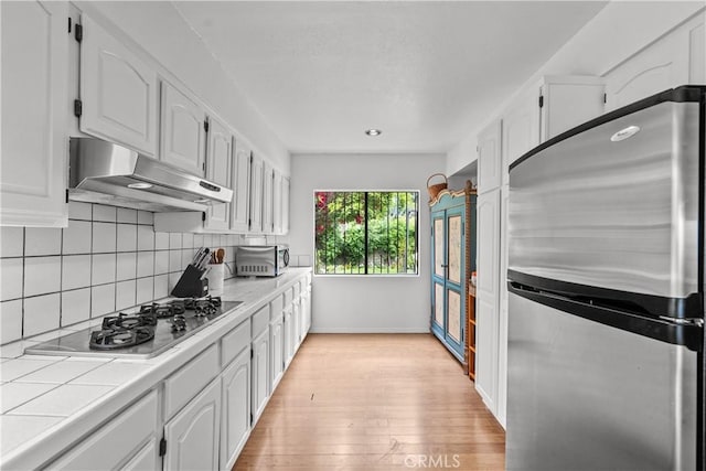 641 Sunnyhill Dr, Los Angeles, CA 90065 - kitchen with appliances with stainless steel finishes, tile countertops, under cabinet range hood, white cabinetry, and backsplash