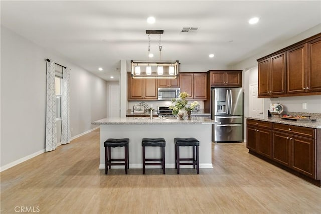 kitchen featuring appliances with stainless steel finishes, a breakfast bar, light wood-style floors, an island with sink, and recessed lighting
