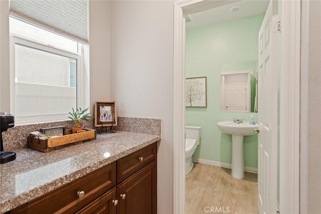 bathroom featuring toilet, wood finished floors, baseboards, and a sink