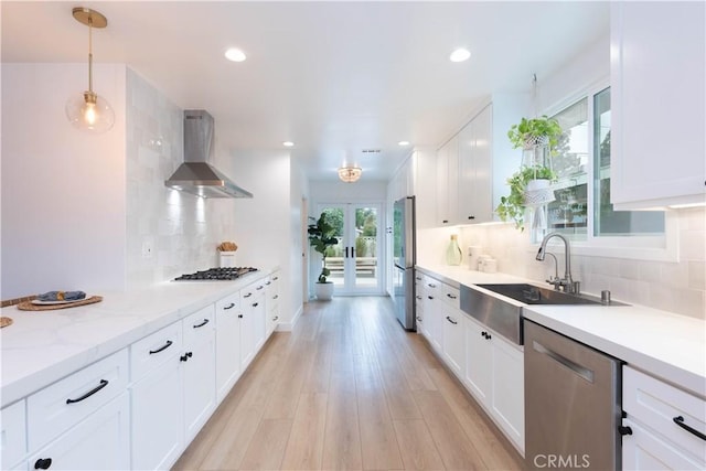 kitchen featuring wall chimney exhaust hood, a sink, appliances with stainless steel finishes, white cabinetry, and recessed lighting