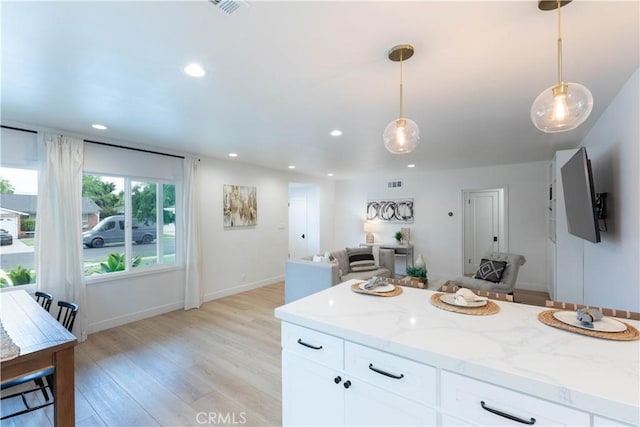kitchen featuring light wood-type flooring, hanging light fixtures, white cabinetry, light stone countertops, and recessed lighting