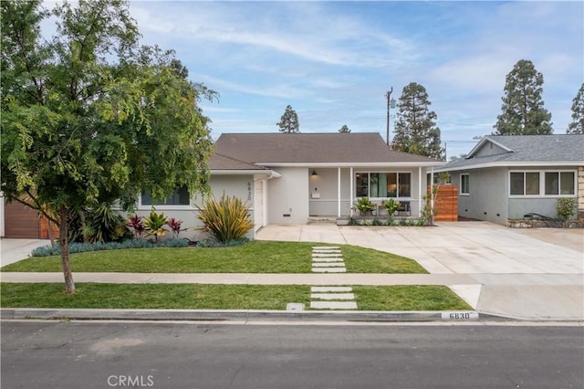 ranch-style home featuring a front yard, a porch, stucco siding, and driveway