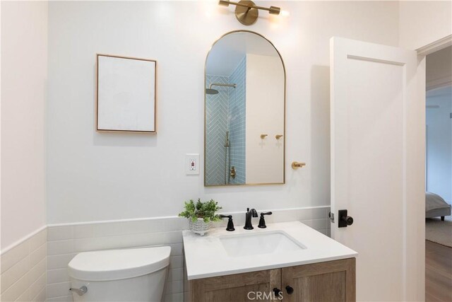 ensuite bathroom featuring vanity, toilet, wainscoting, and tile walls