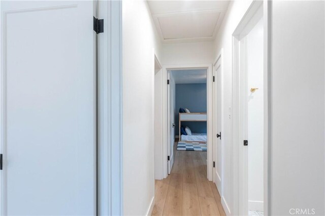 corridor featuring light wood-style flooring, attic access, and baseboards
