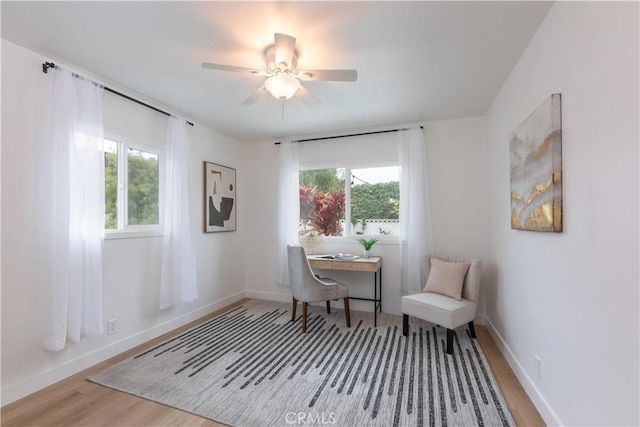 sitting room with wood finished floors, a desk, ceiling fan, and baseboards
