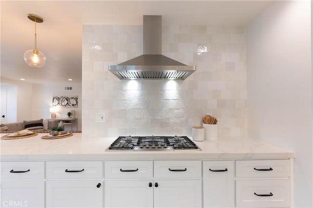 kitchen with wall chimney exhaust hood, stainless steel gas stovetop, white cabinetry, backsplash, and light stone counters