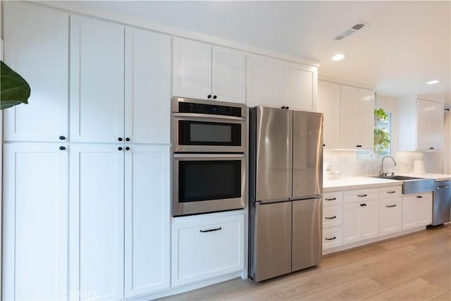 kitchen with appliances with stainless steel finishes, a sink, light wood-style floors, white cabinetry, and light countertops