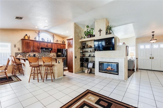 kitchen with lofted ceiling, black fridge, a peninsula, under cabinet range hood, and light tile patterned floors