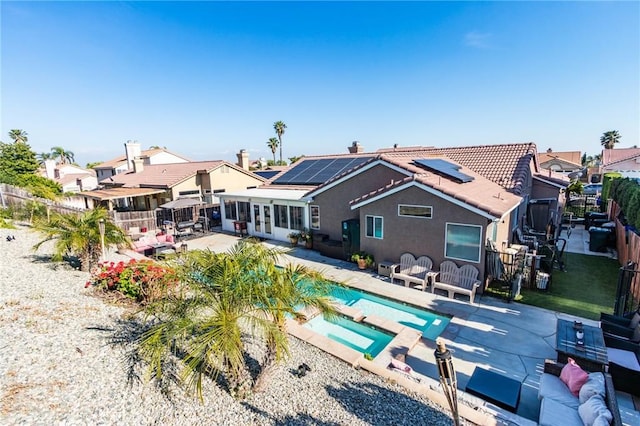 back of house with roof mounted solar panels, a patio area, and a fenced backyard