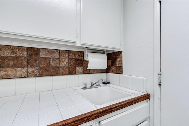kitchen view of tile countertops, white cabinetry, a sink, and backsplash
