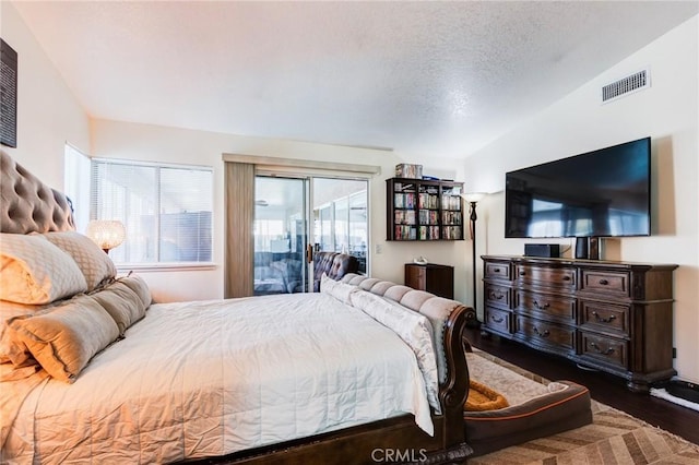 bedroom with access to outside, lofted ceiling, wood finished floors, and a textured ceiling