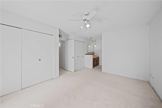 unfurnished bedroom featuring light carpet, a ceiling fan, and connected bathroom