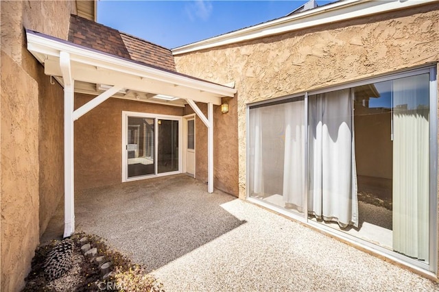entrance to property with a patio, stucco siding, and a shingled roof