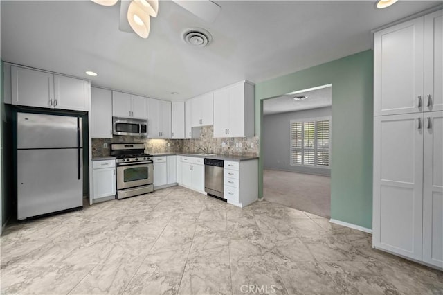 kitchen featuring appliances with stainless steel finishes, tasteful backsplash, a sink, white cabinets, and light marble finish floors