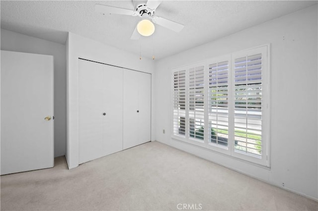 unfurnished bedroom featuring carpet, a closet, a textured ceiling, and ceiling fan