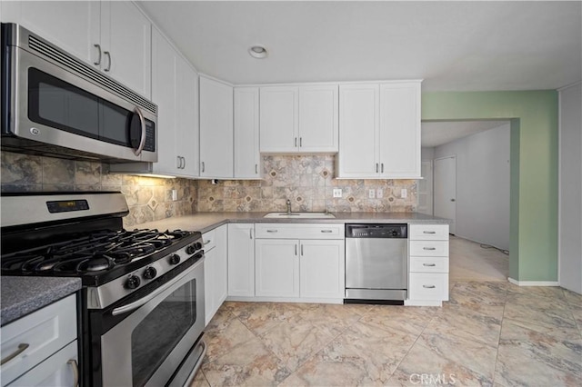 kitchen featuring appliances with stainless steel finishes, a sink, backsplash, white cabinetry, and baseboards