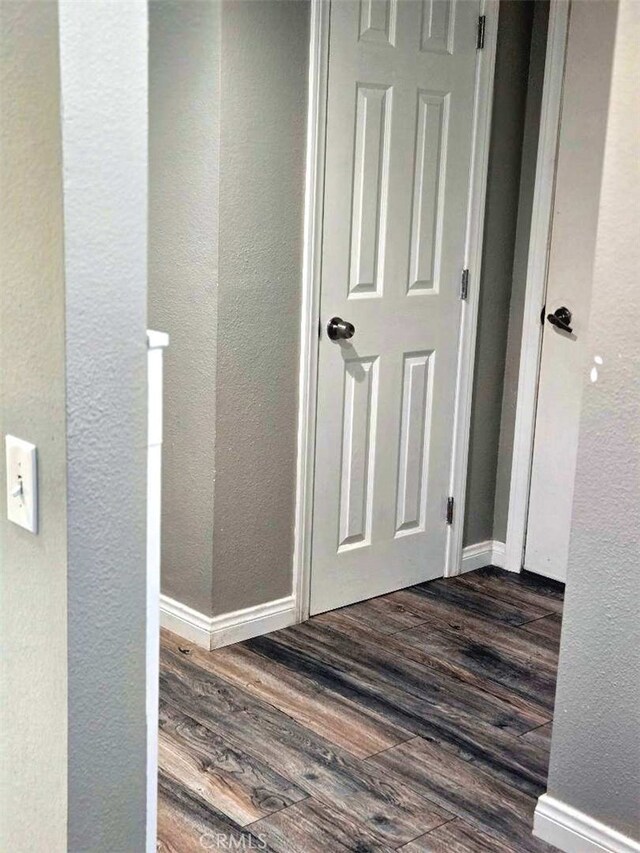 corridor featuring dark wood-style floors, a textured wall, and baseboards