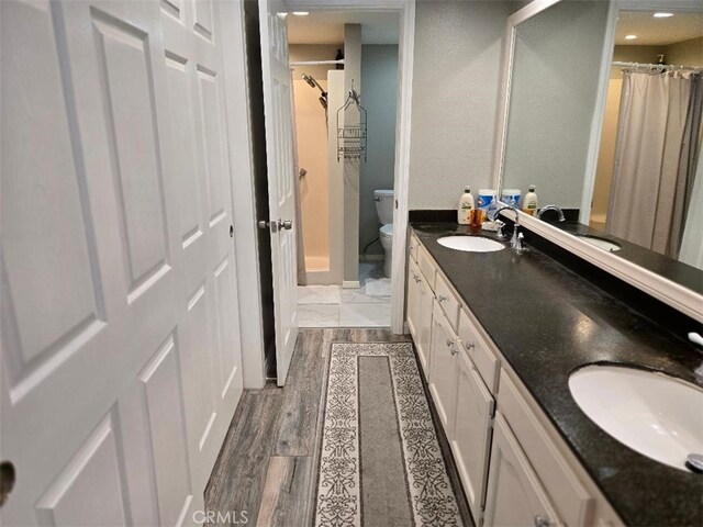 full bathroom with double vanity, toilet, and wood finished floors