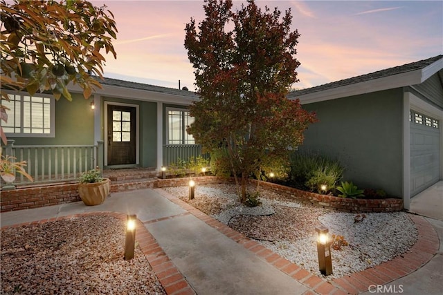 6911 E 10th St, Long Beach, CA 90815 - exterior entry at dusk featuring stucco siding, a porch, and a garage
