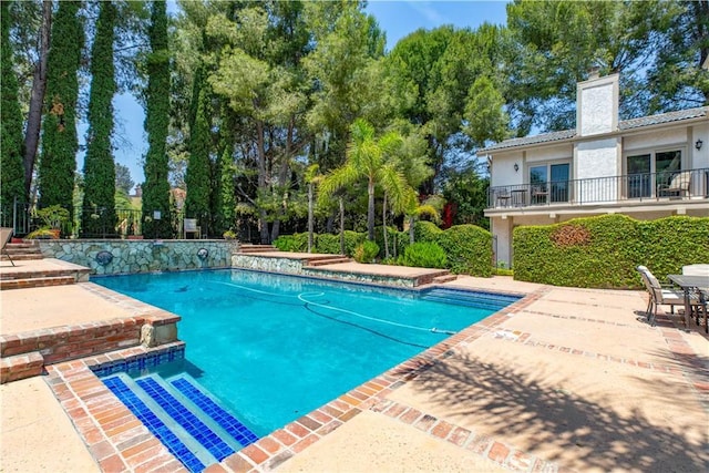 swimming pool featuring a patio and view of scattered trees