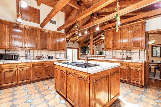 kitchen with black electric stovetop, stainless steel microwave, tile counters, decorative backsplash, and a center island