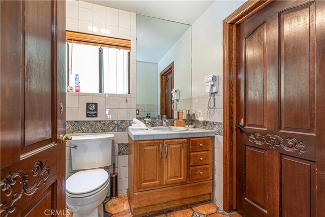 bathroom with tile walls, toilet, tile patterned flooring, vanity, and wainscoting