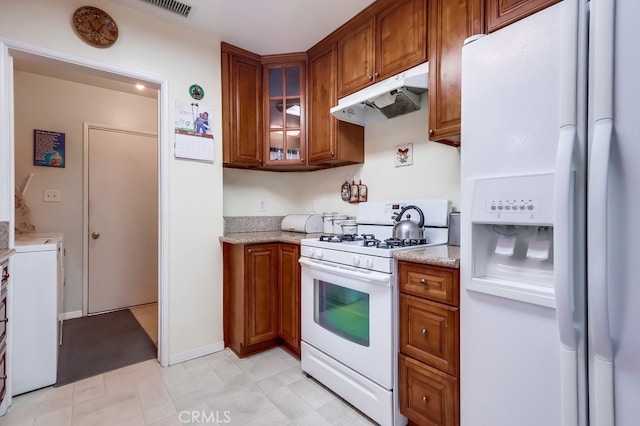 kitchen featuring white appliances, under cabinet range hood, brown cabinetry, and glass insert cabinets