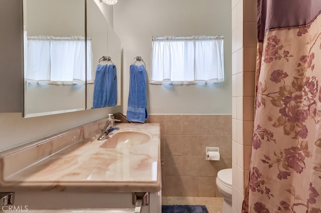 bathroom featuring toilet, vanity, tile walls, curtained shower, and a wainscoted wall