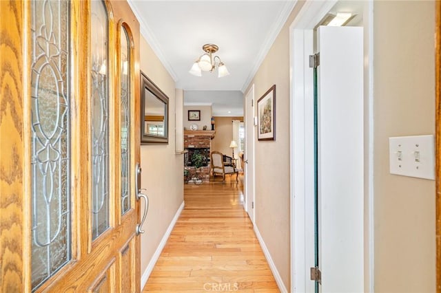 hallway with light wood-style flooring, crown molding, baseboards, and a chandelier