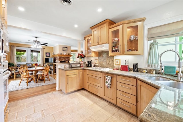 kitchen with a sink, under cabinet range hood, light brown cabinetry, a peninsula, and light stone countertops