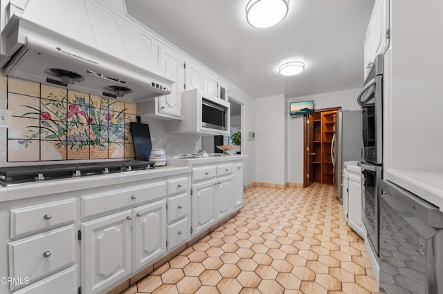 kitchen with under cabinet range hood, stainless steel appliances, white cabinets, and tile counters