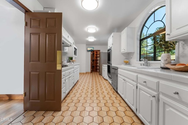 kitchen with tile counters, a sink, and white cabinets
