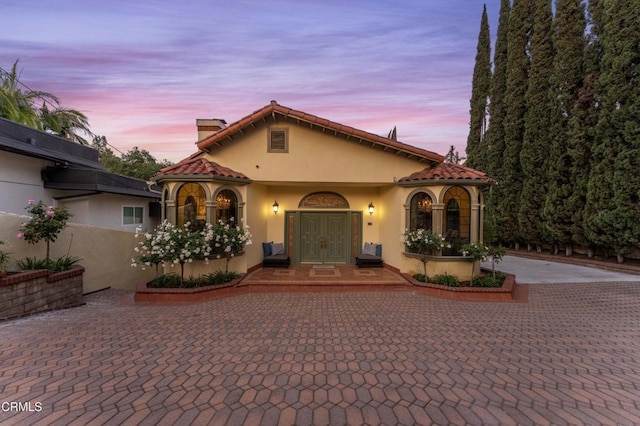 mediterranean / spanish-style home with stucco siding, a chimney, curved driveway, and a tiled roof