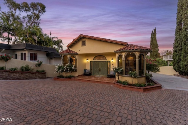 mediterranean / spanish home featuring stucco siding, curved driveway, fence, and a tile roof