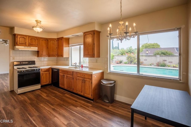 kitchen featuring white range with gas stovetop, under cabinet range hood, a sink, dark wood-type flooring, and baseboards