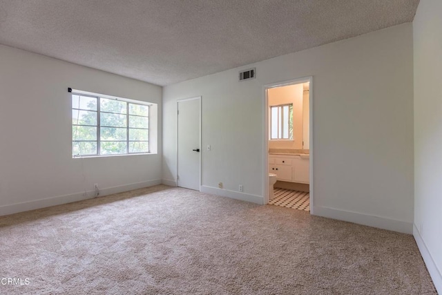 unfurnished bedroom with carpet, a textured ceiling, baseboards, and connected bathroom